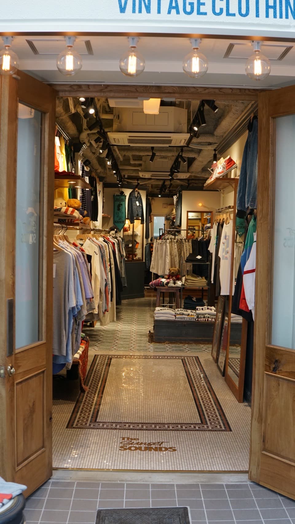 Inside Koenji PAL Shopping Street. Secondhand clothes are displayed on fixtures on both sides.
